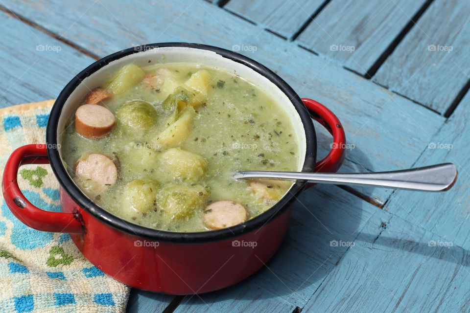 Soup with sausage and potatoes in a red pot on a blue table