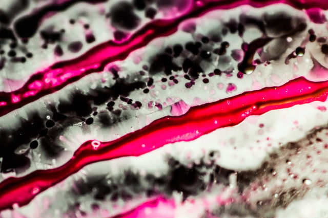 Black and pink refill ink spilled onto the white sink and the ink mixed into abstract blobs and patterns.