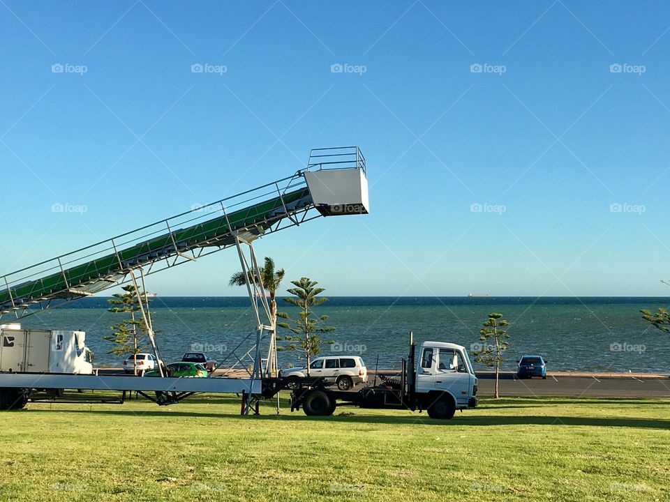 Crane on truck bed raised against a cloudless blue summer sky at ocean