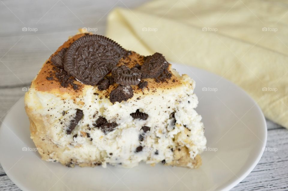 Oreo cookie cheesecake on a white plate with a yellow towel in the background