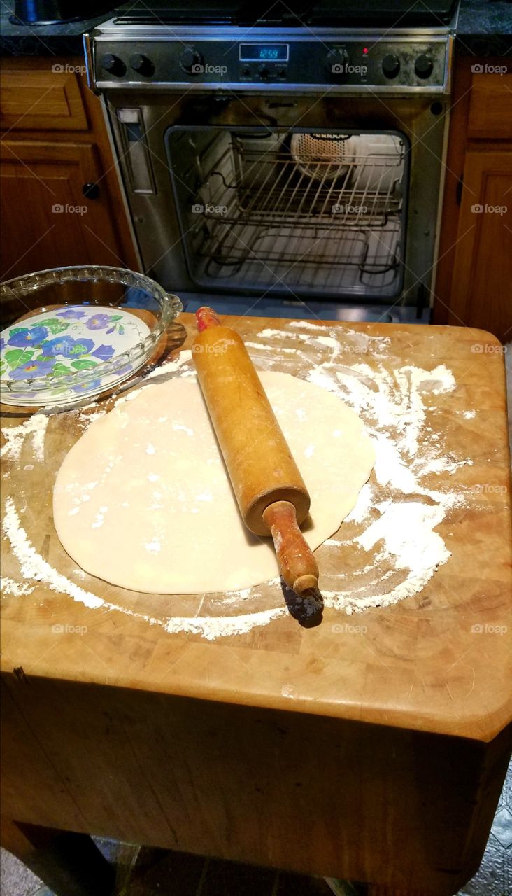 Rolling out pie crust on floured wood table using rolling pin. Working under good light with oven nearby