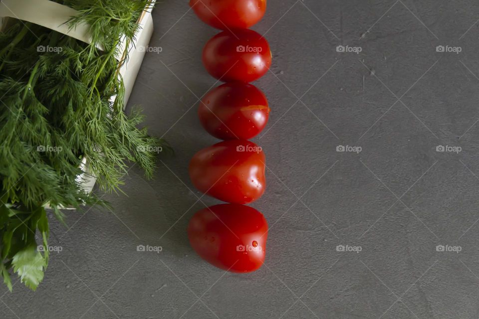 Fresh, bright, juicy vegetables and herbs for preparing salads and other vegetable dishes are on a gray, kitchen worktop.
