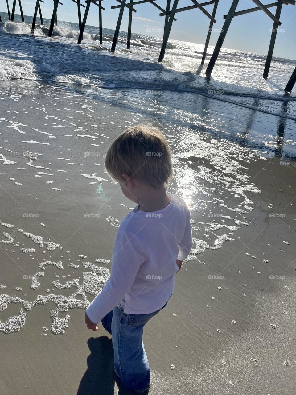 Warm sunshine glistening over water with Toddler touching his toes in The Atlantic Ocean for the very first time. 