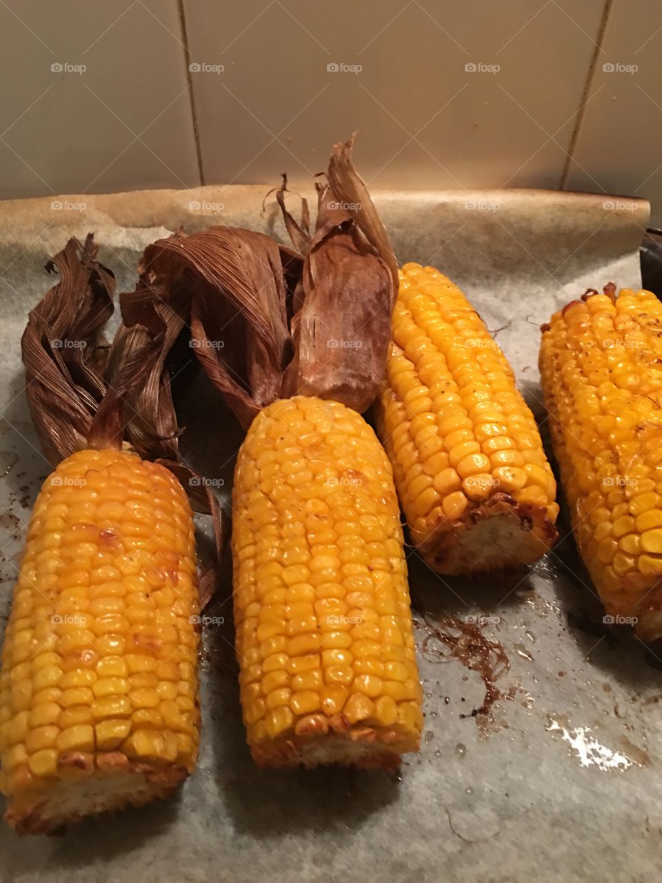 Four roasted yellow juicy corncobs husks pulled back and just out of the oven