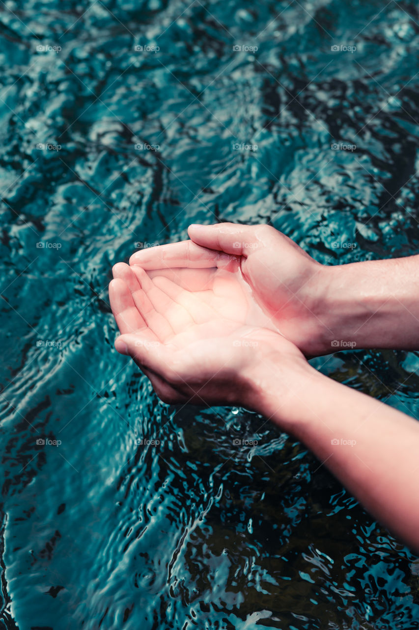 Young boy taking pure water from a river and holding it in the hands. Closeup of hands holding a clean water