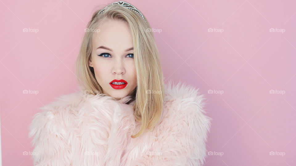 Blond glamour princess girl in crown on pink background 