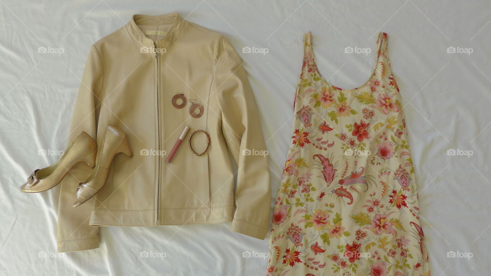 flat lay beige leather jacket, floral dress, gold shoes, copper jewelry