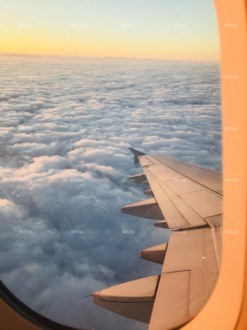 Airplane window seat views showing the warm glow of the sun from above the clouds. 
