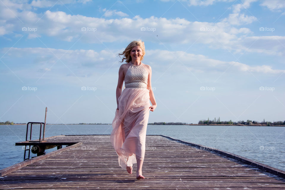 girl in beautiful gown running. girl in beautiful evening gown running on a deck at lake