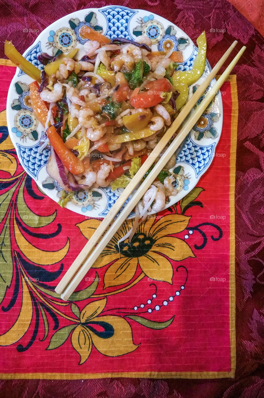 Prawn and vegetable stir fry with sweet chilli sauce on a colourful table mat