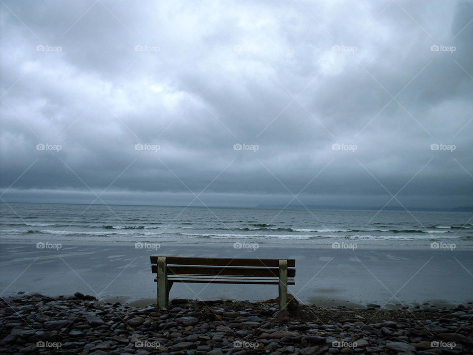 View of bench and sea against storm cloud