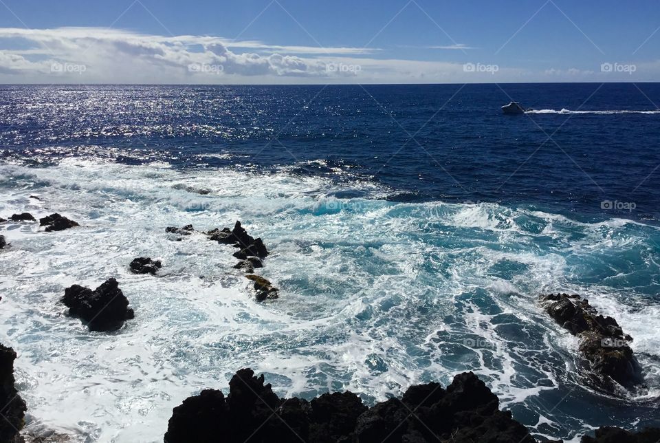 Sea foam and blue ocean waves with a boat in the distance 