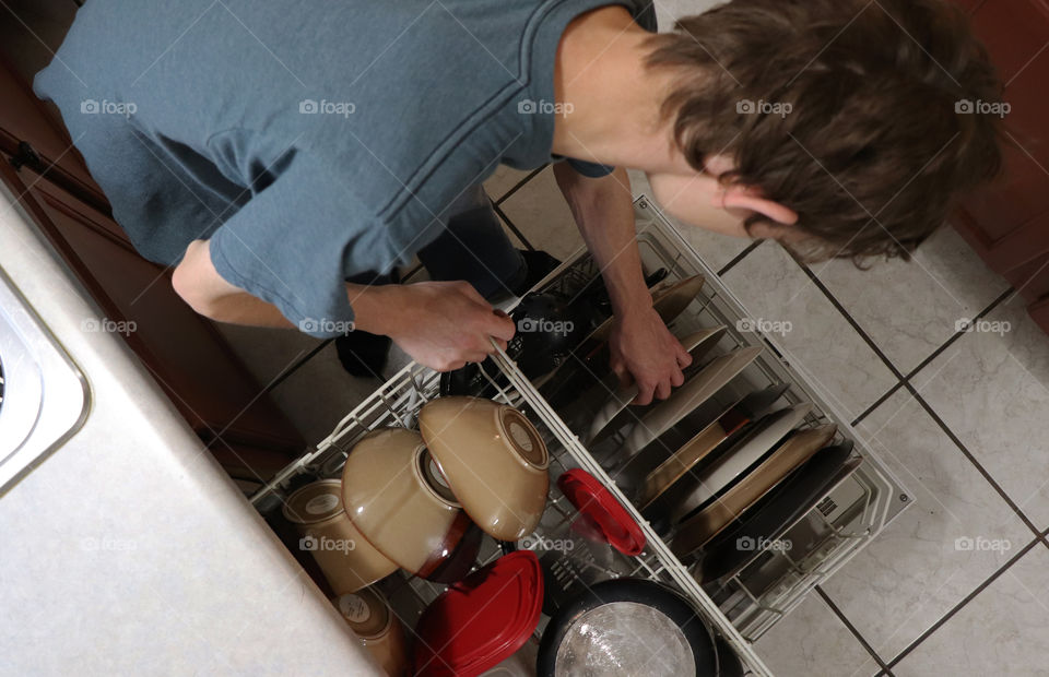 Young teenage boy unloading the dishwasher