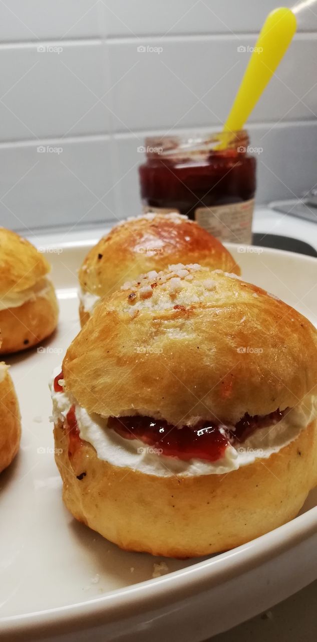 Four cardemom breads filled with strawberry jam and whipped cream. Some sugar on the top of the buns.