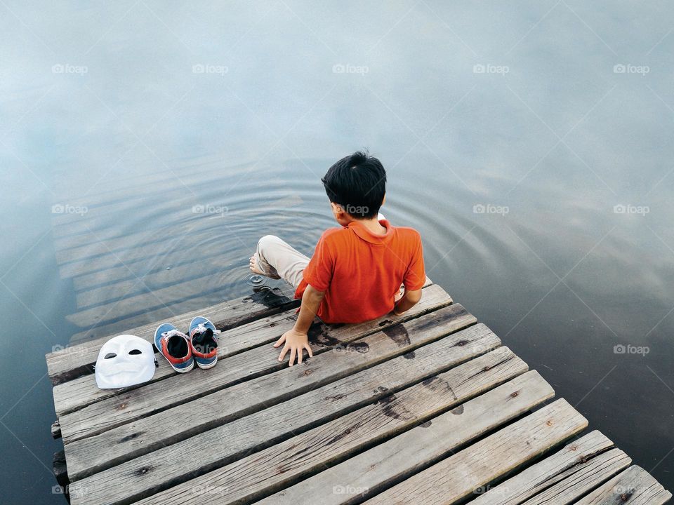 A boy is dipping his feet in the calm water to make ripples