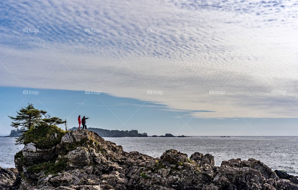 Dad and daughter on a rocky outcropping and looking at the vast expanse of the Pacific Ocean 