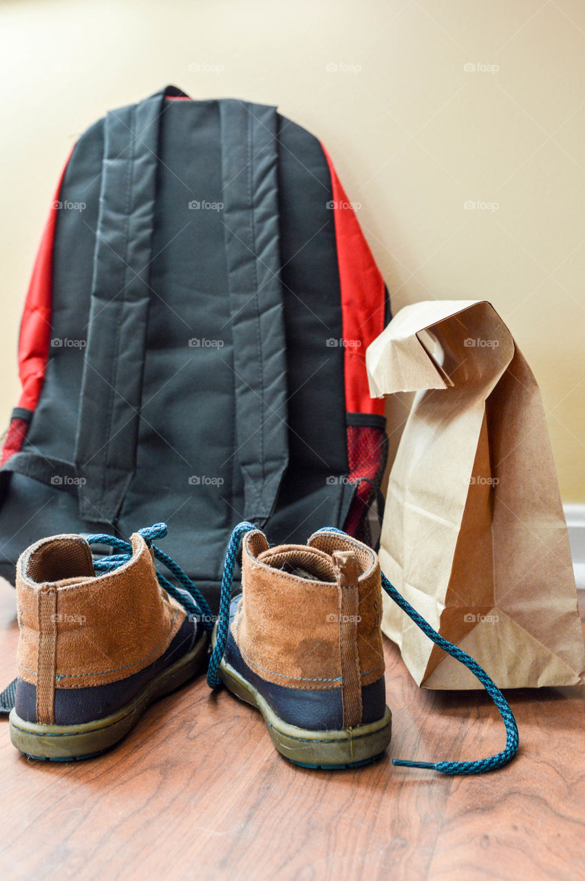 Backpack, shoes and brown paper bag lunch laid out and ready for school