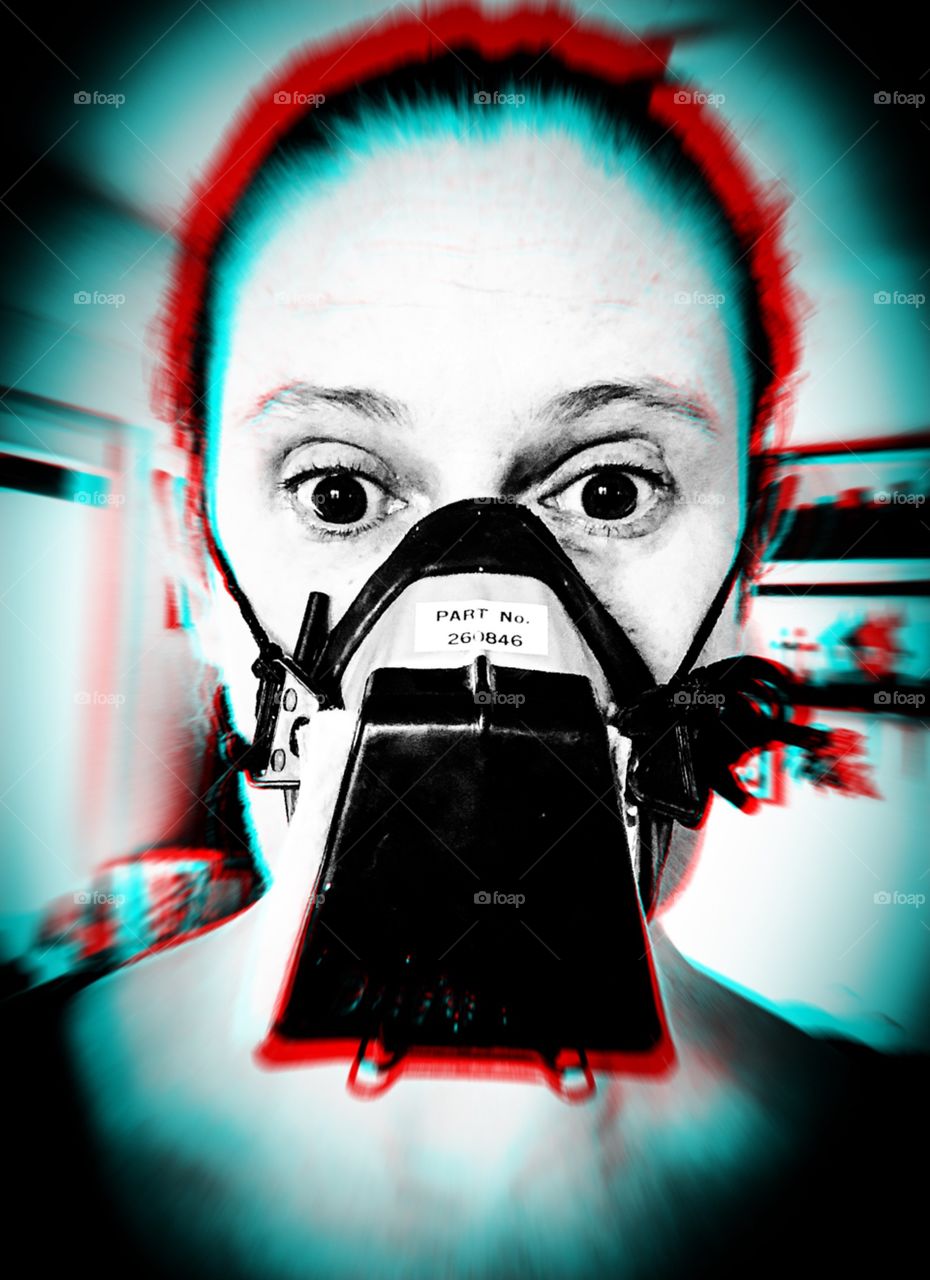 A woman with a look of shock in her eyes is wearing a dust mask, in black and white with red distortion 