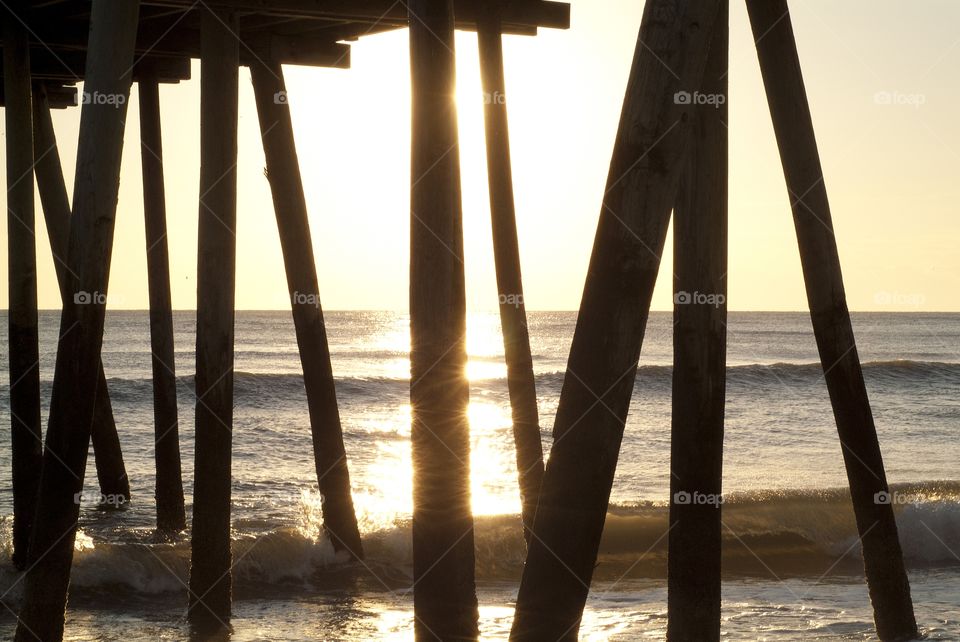 Wooden posts from a jetty walk above catch the suns light during a sunrise on the beautiful shore of Virginia beach.
