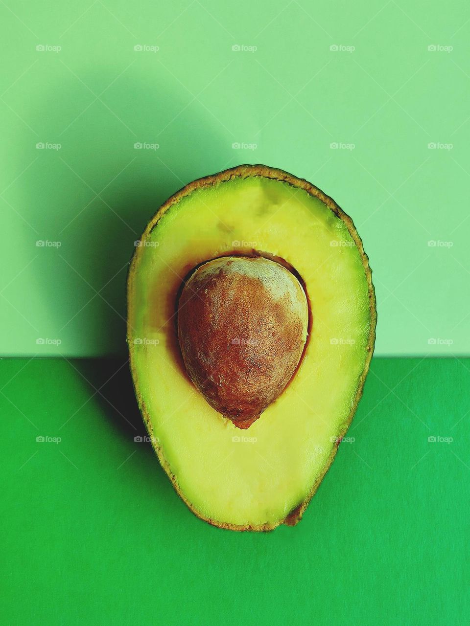 Colors.  Half of a green kiwi with a brown bone lies on the backgrounds of mint green and dark green colors