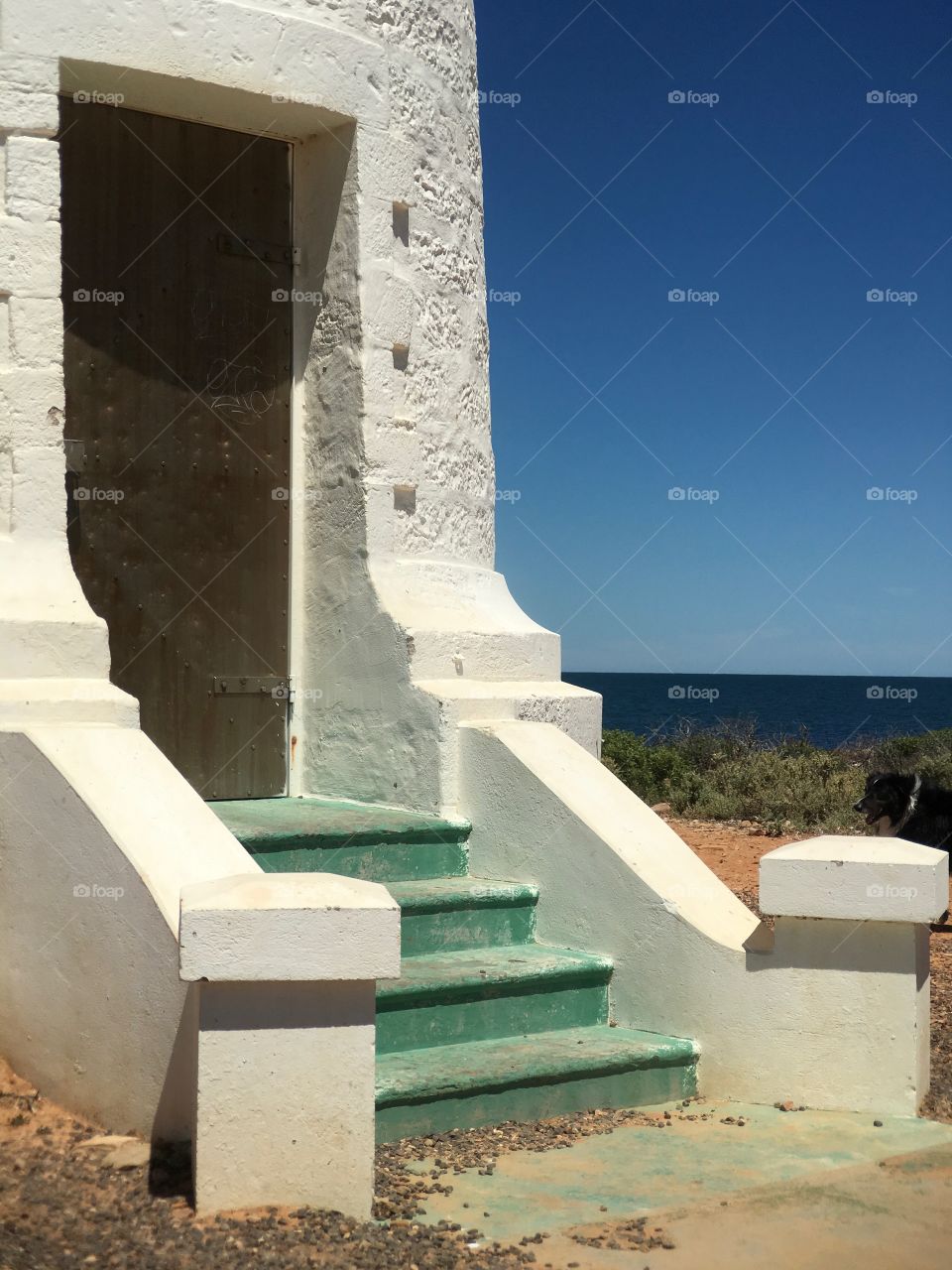 Lighthouse door and steps white stone heritage lighthouse against a vivid blue sky and ocean 