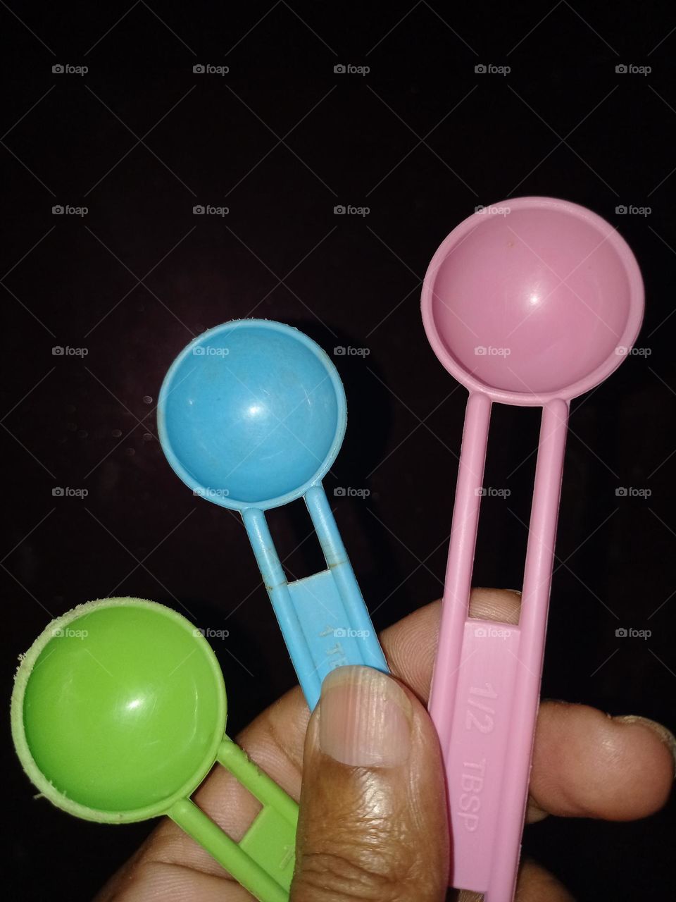 A young man holding multicolour plastic spoons green blue and pink colour it's looks amazing with nice background