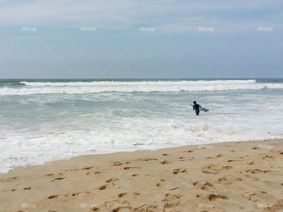 Beaches vacation for surfers is paradise. A man, surfboard in hand, enters the water determined to practice his sport in complete freedom facing the immensity of the ocean.