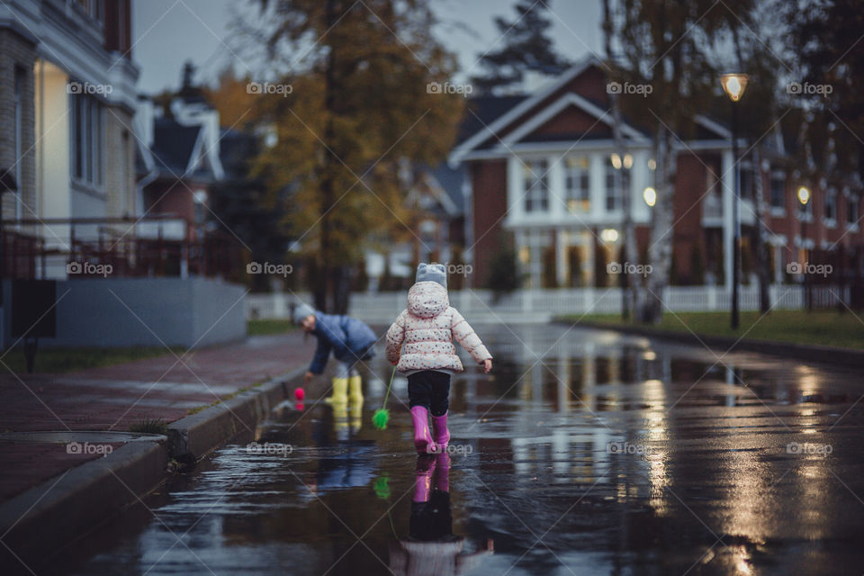 Little girl  in waterproof boots playing in a puddle 