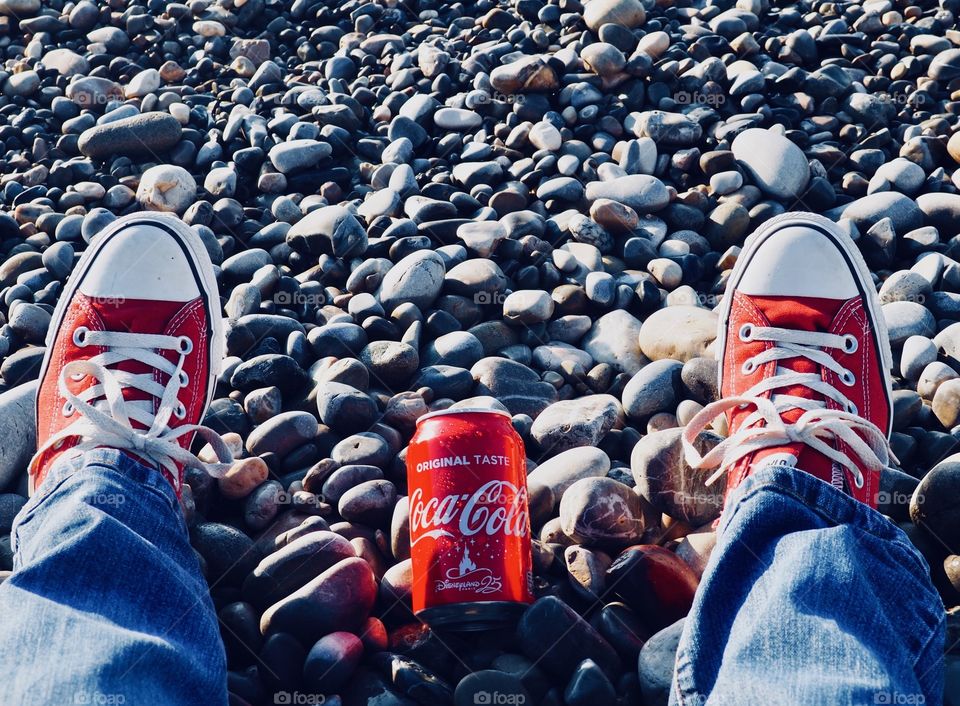 A can of Coca Cola on the beach with red sneakers.