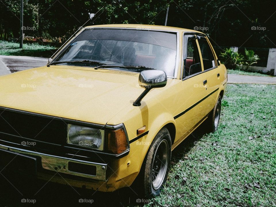 Yellow classic toyota dx parked in the front yard