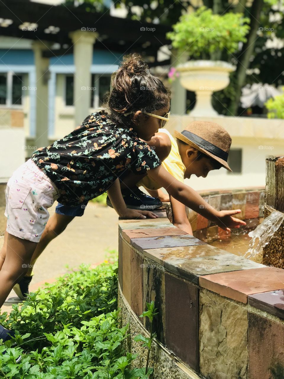 Kids in summer outfits and playing near water fountain with flowing water.