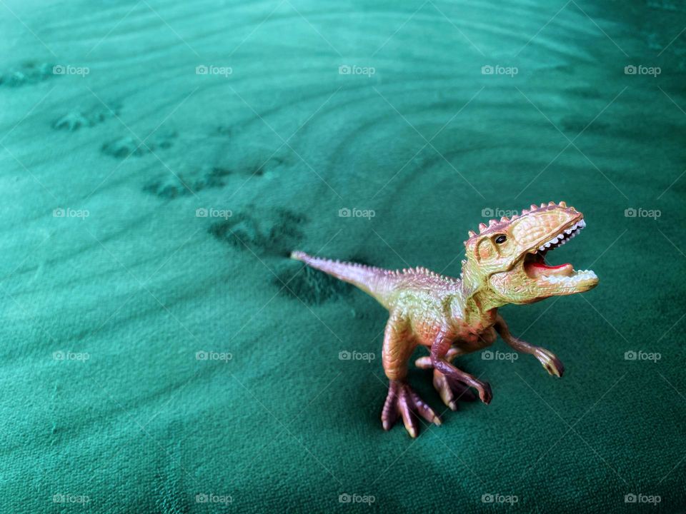 Toy dinosaur leaving footprints on a green blanket 