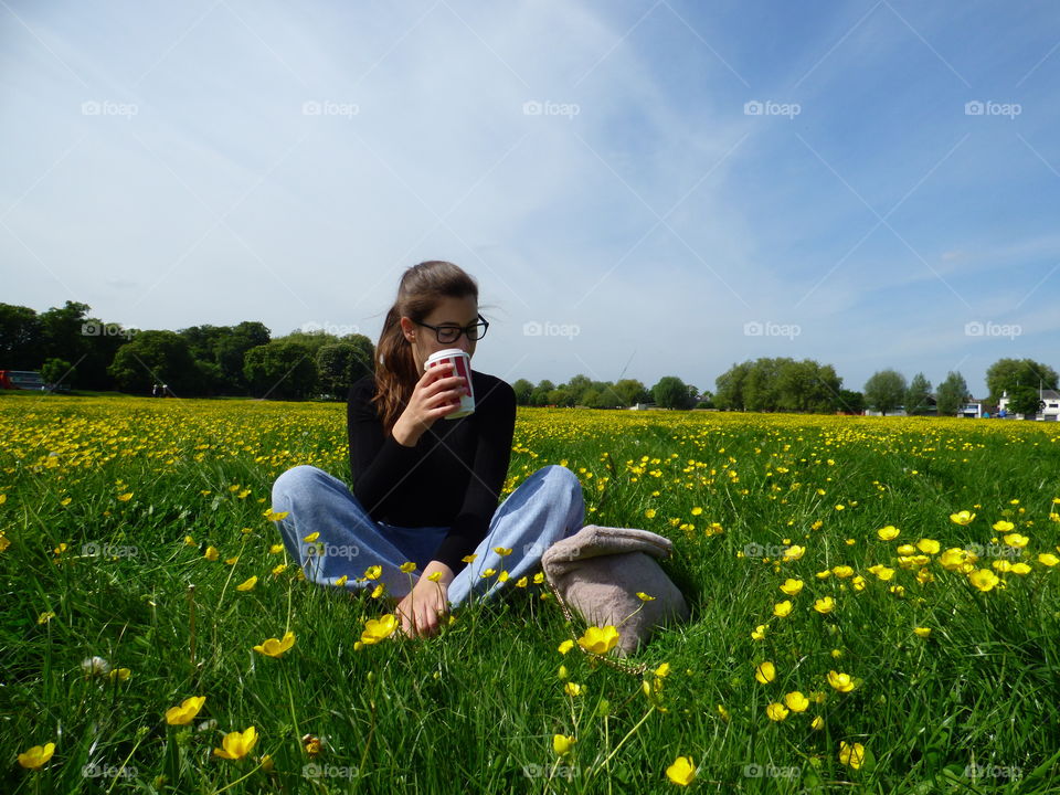 girl drinking coffee sitting on the grass covered in dandelions
