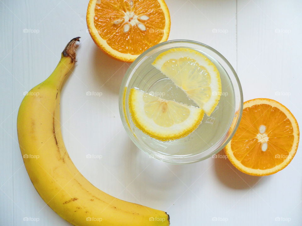 a glass of lemonade with lemon, bananas and sliced ​​oranges on a white background