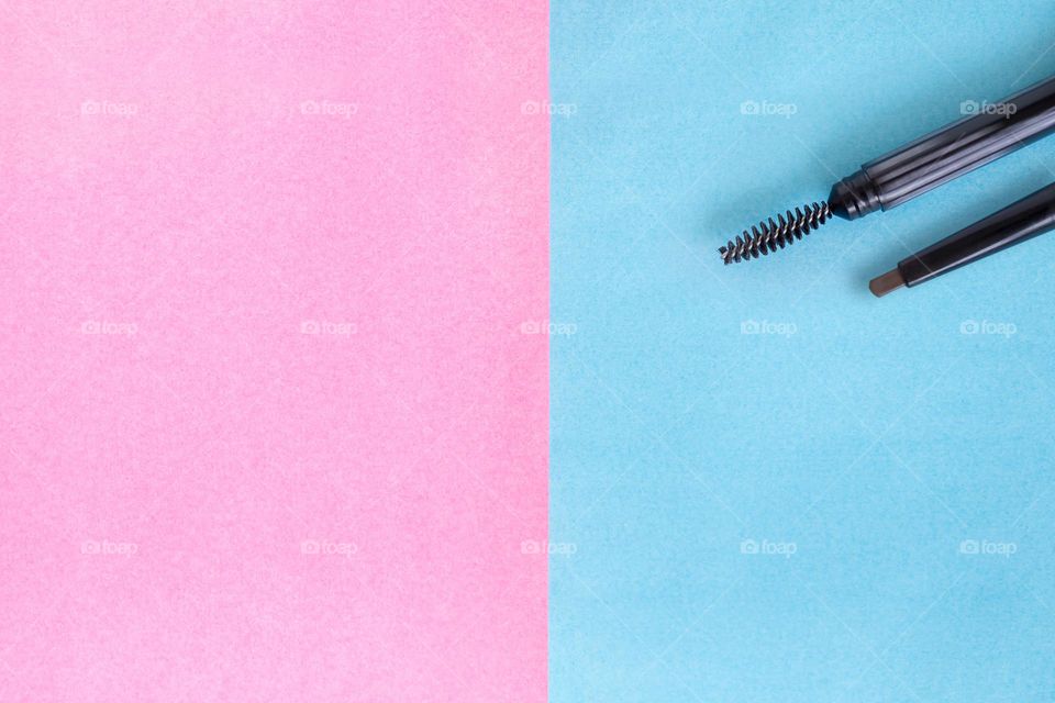 Eyebrows pencil and brush, makeup flatlay on pink and blue background with copy space