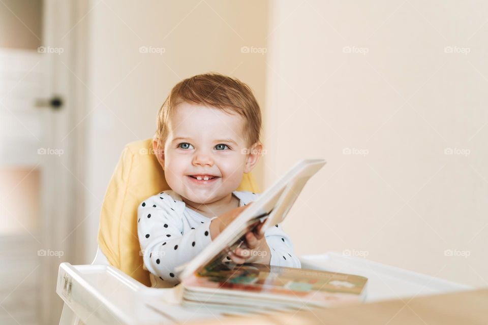 Happy cute baby girl reading a book at home 