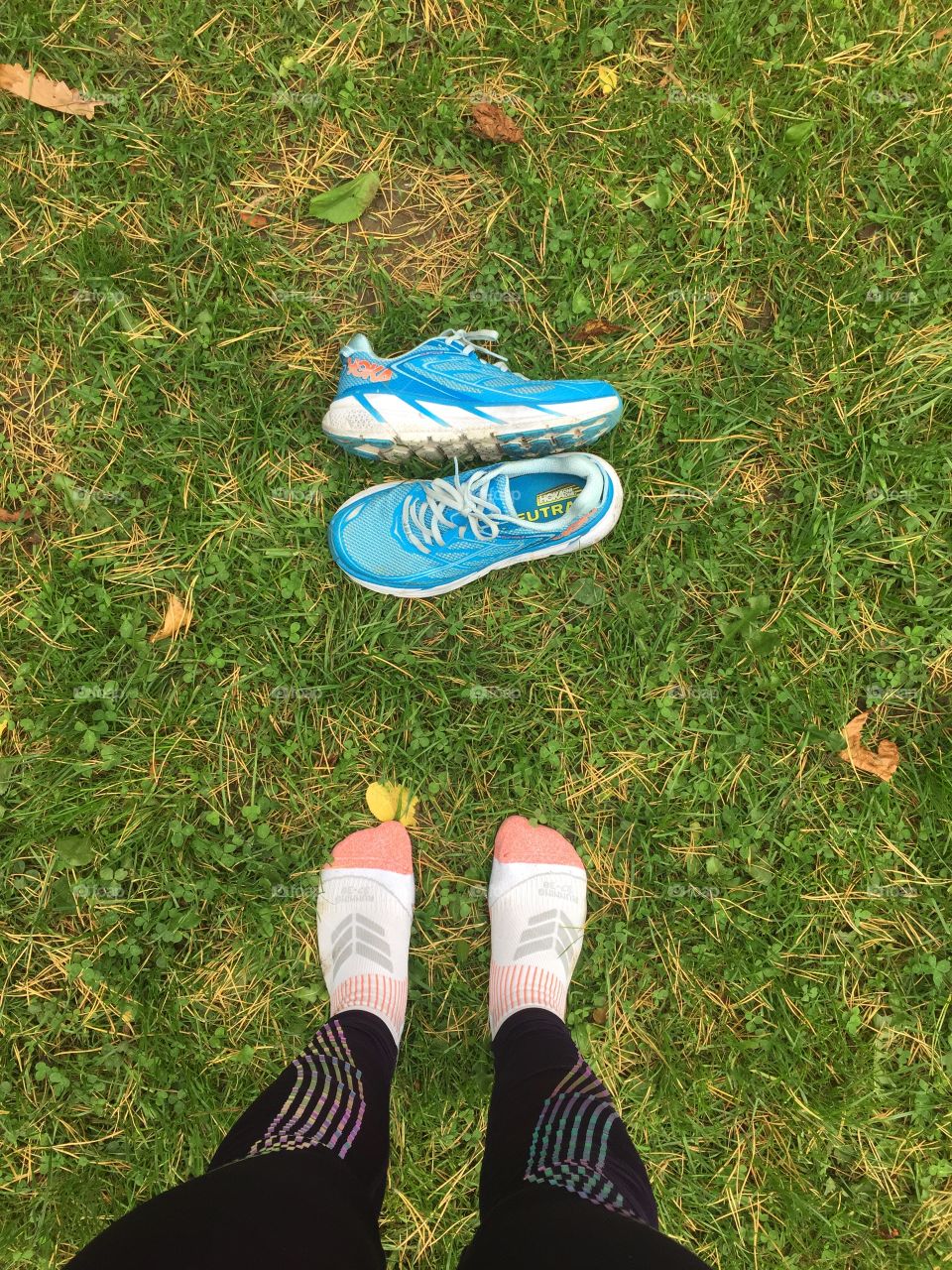 Feet and blue hoka running shoes on green grass