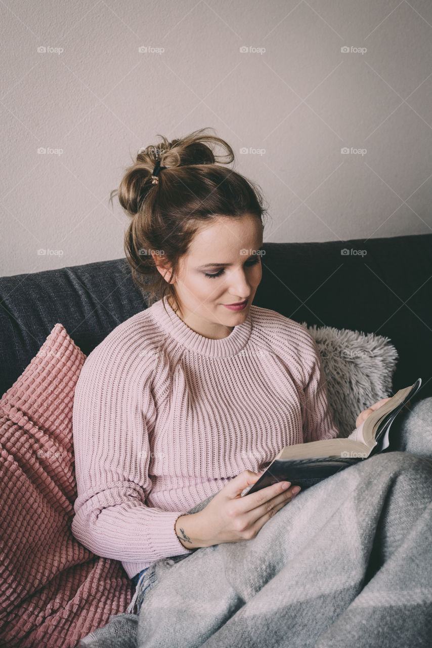 Young woman reading a book in her bed. Sweater weather.