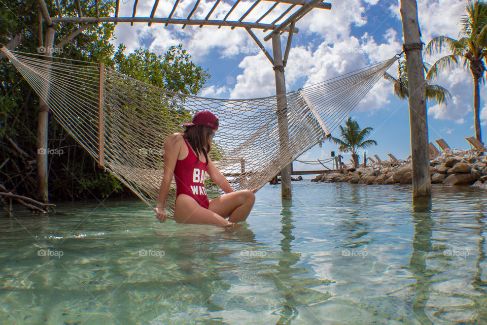 Girl in red one piece posing seductively on hammock above shallow water