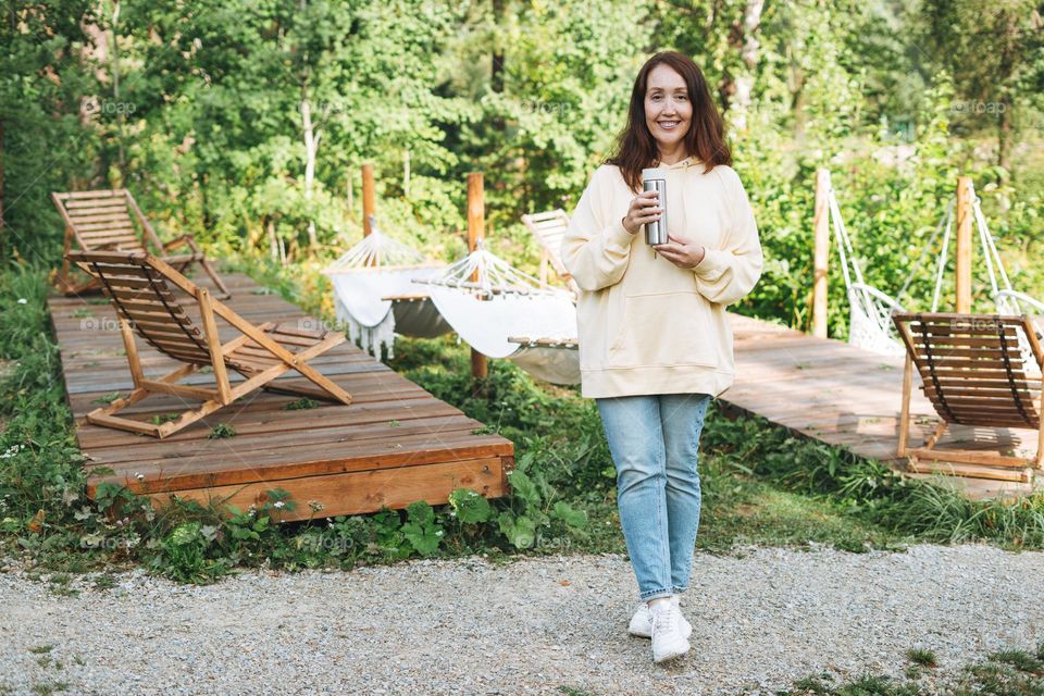 Young brunette woman in casual drinking tea and relaxing in camping in nature
