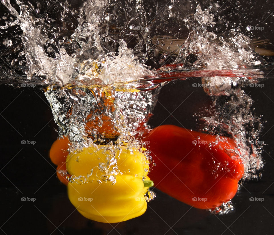 Yellow, orange, and red bell peppers splashing into water 