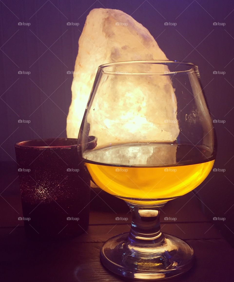 Glass of whiskey in brandy glass with candle in red holder and salt lamp in the background 