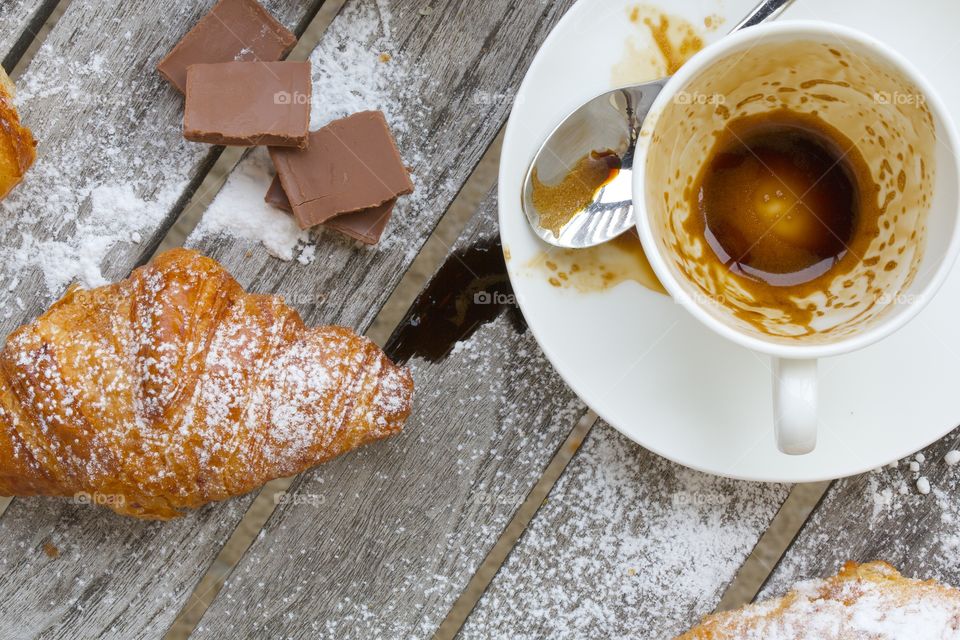 Croissant, pieces of milk chocolate, and empty coffee cup on a wooden surface. Flat lay.