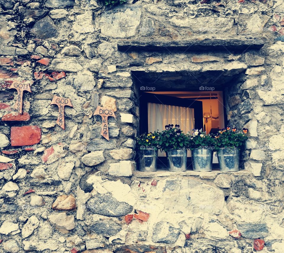 Open window with flower pots on the sill. Stone wall as a background
