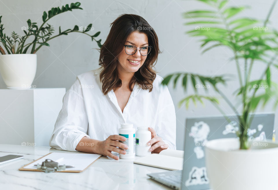 Young woman plus size body positive brunette doctor in glasses using laptop in office room 