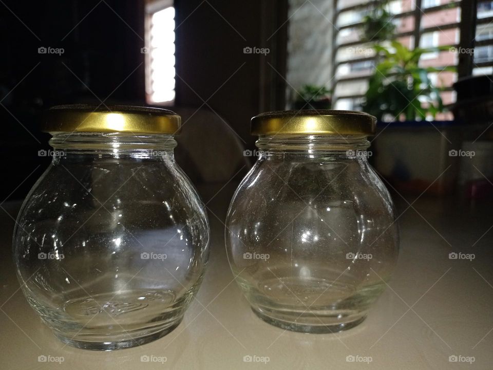 Two glass jars on the table with goldan colour cap nice blur background of window it was looking like a tweens brothers