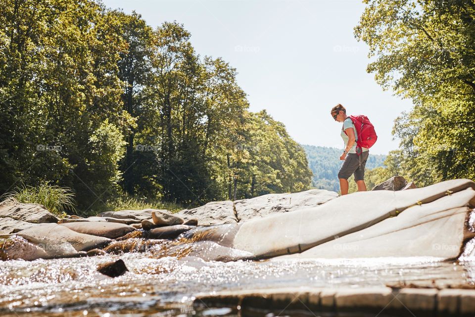 Bieszczady Mountains. Trekking with backpack concept image. Female backpacker wearing trekking boots crossing mountain river. Woman hiking in mountains during summer trip. Vacation trip close to nature. Natural scenery. Poland