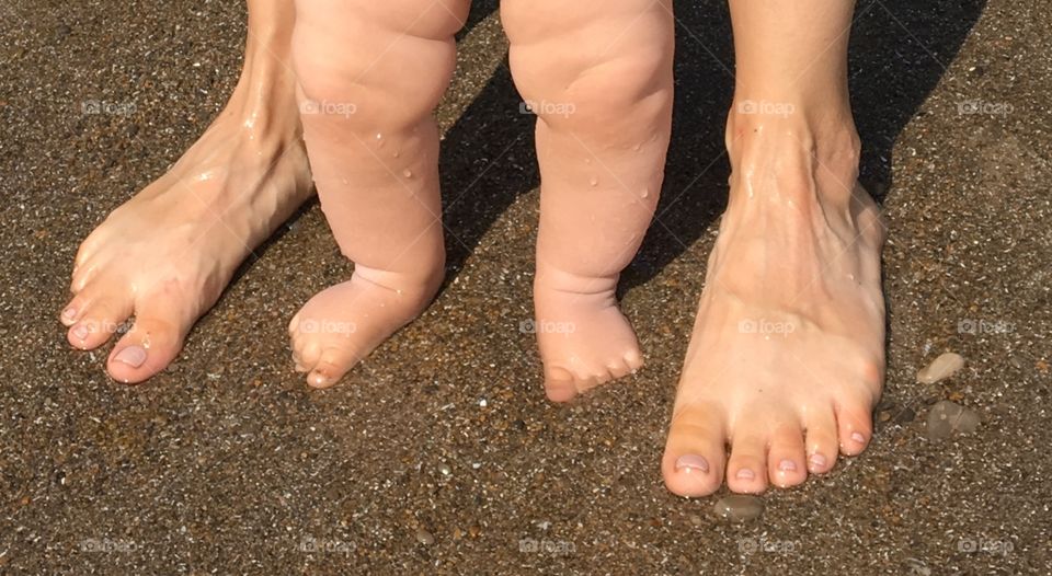 Mother and Baby stand barefoot in the wet sand waiting for another wave at the beach. 