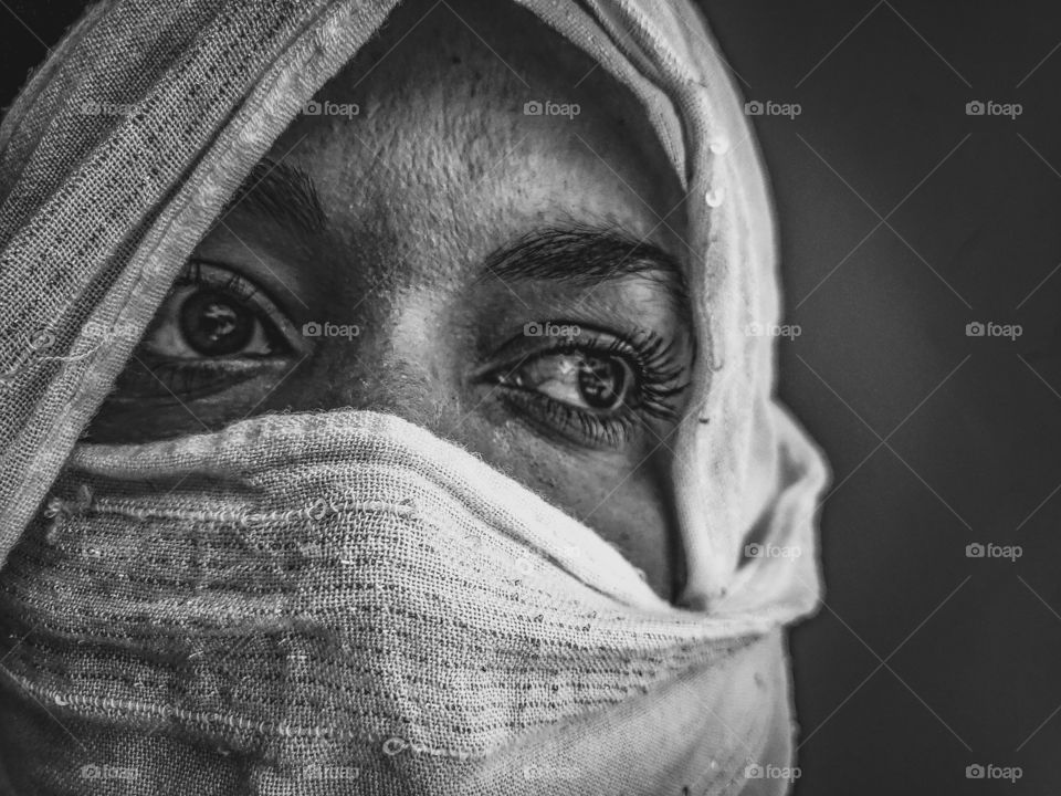 Black and white portrait of a women protecting her face and head with a white scarf from the 2020 corona virus while looking away concerned and overwhelmed by the pandemic.