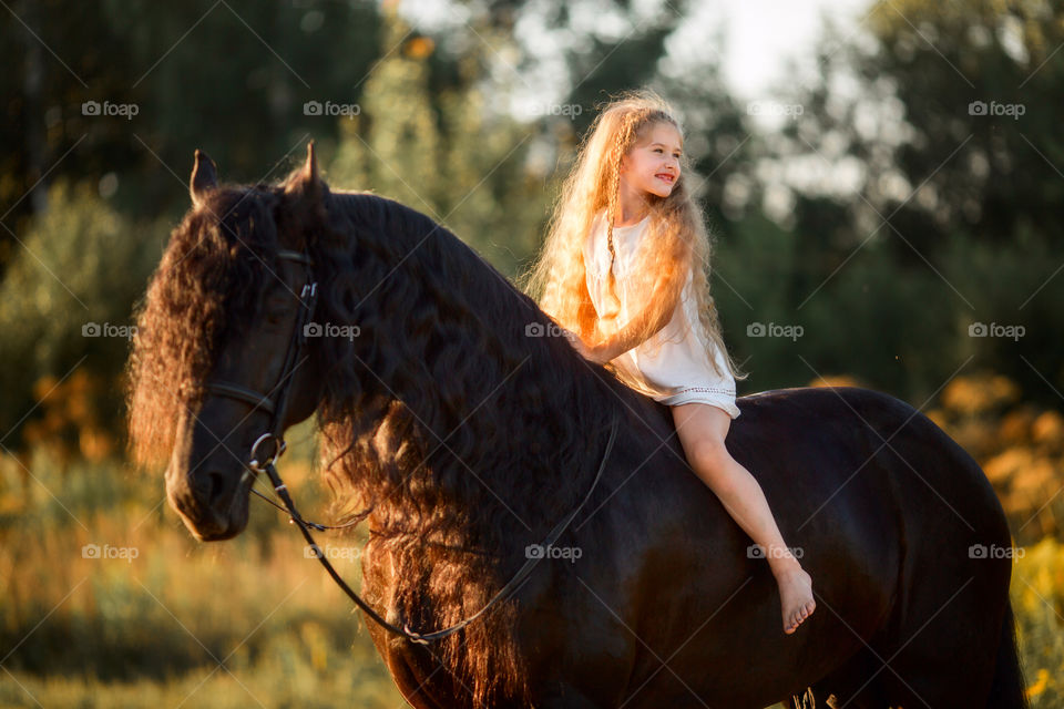 Little girl with black fresian stallion at summer evening 